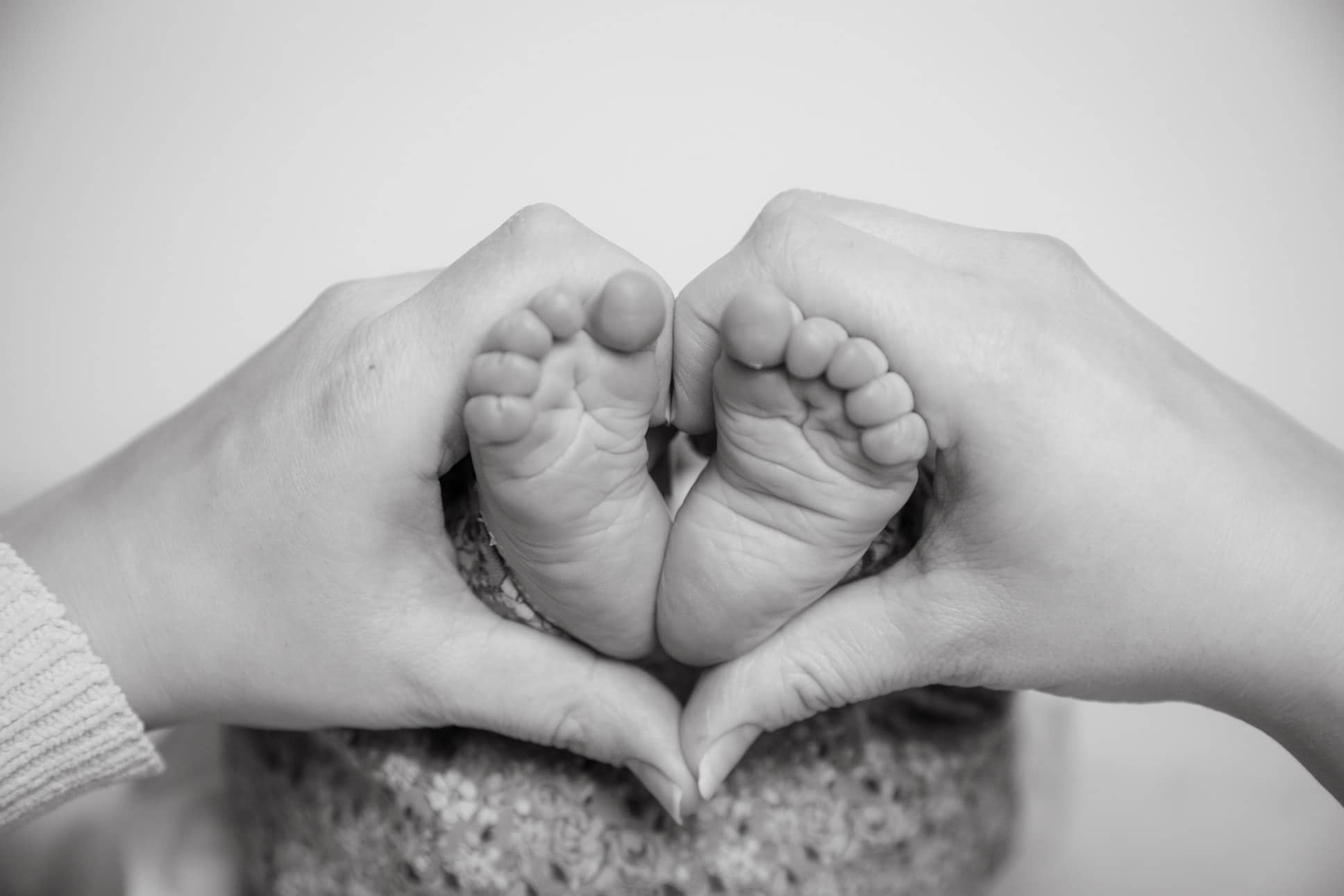 a new born baby feet and an adult hand making a heart