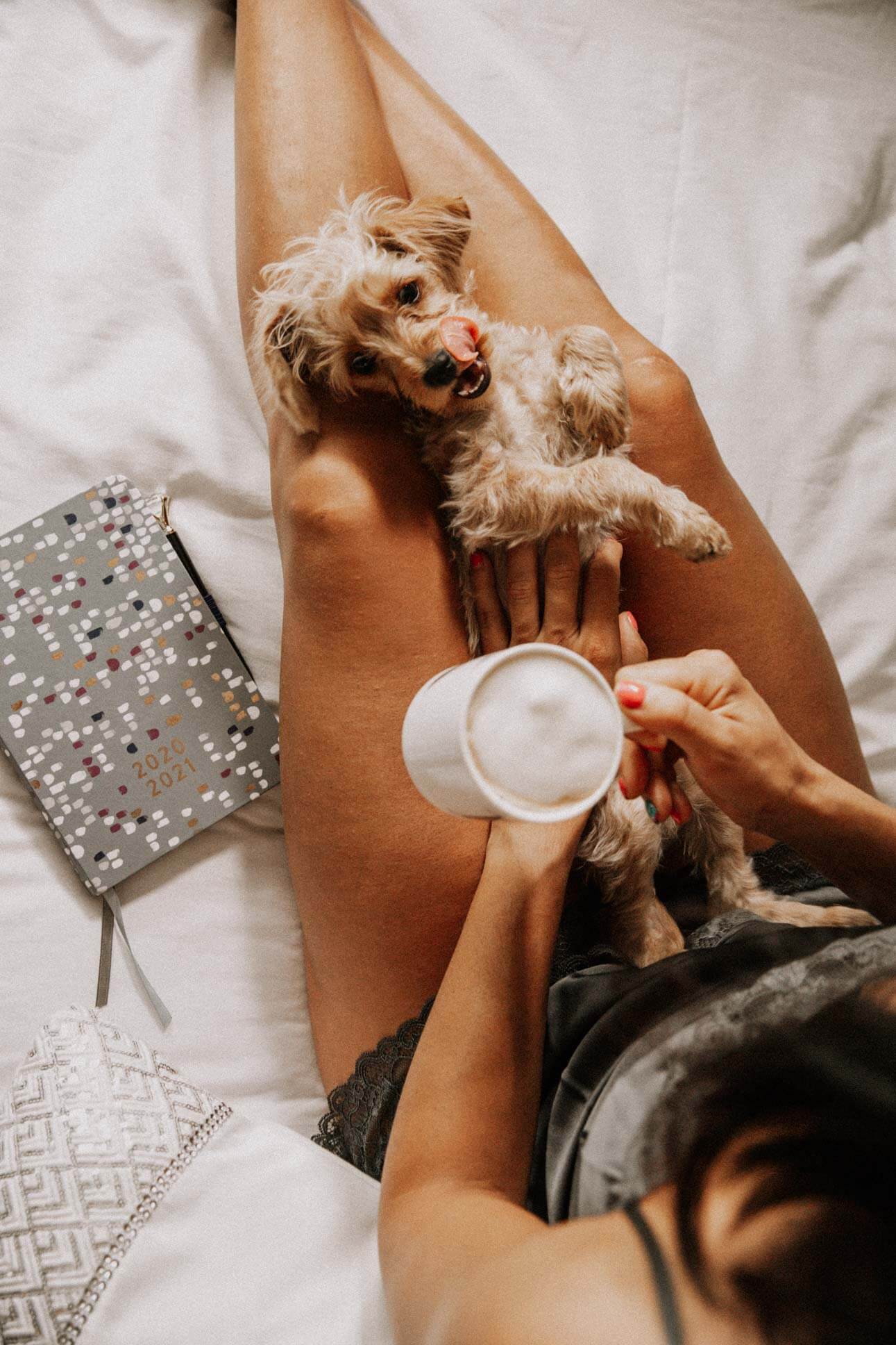 a lady on a bed holding a coffee with a dog